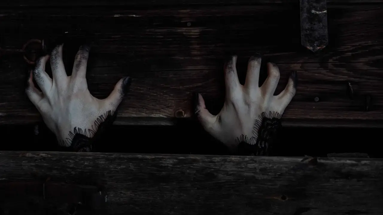 Mains pâles aux doigts noircis sortant d'une caisse en bois sombre, évoquant une musique qui fait peur au piano.
