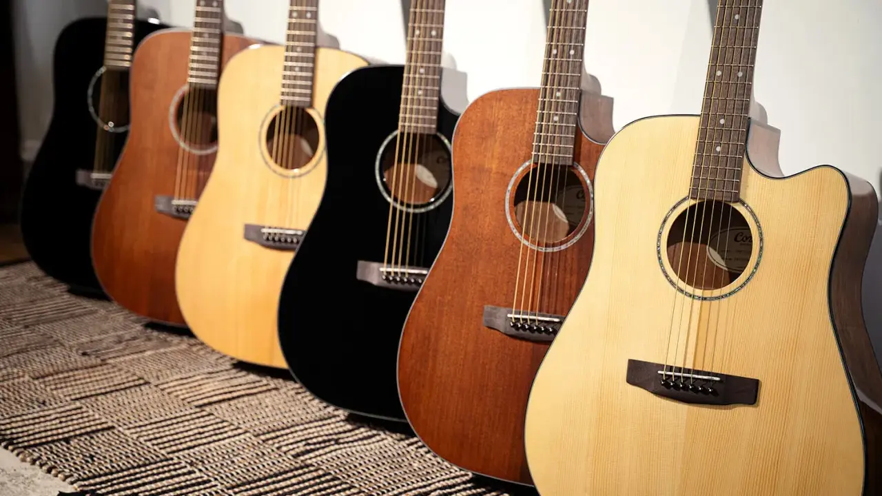 Une rangée de guitares acoustiques Cort, noires, marron et naturelles, posées sur un tapis rayé.