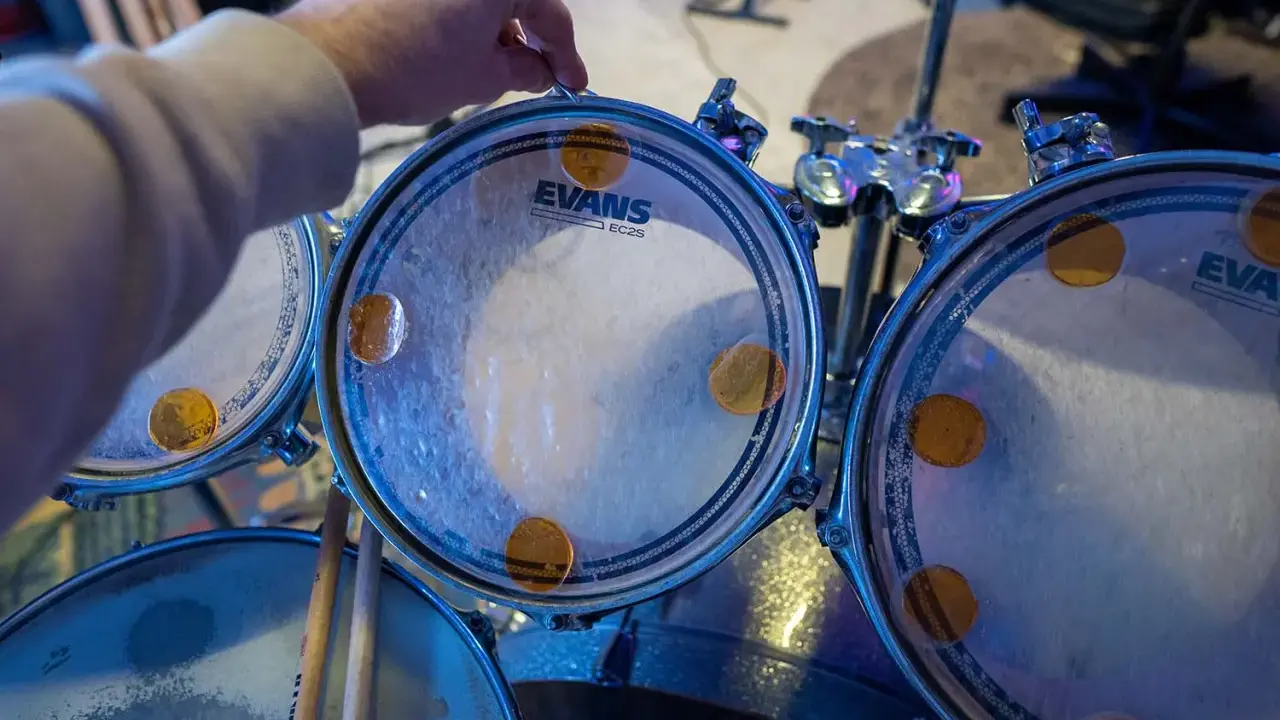 Main d'un batteur ajustant un timbre sur une peau de batterie Evans, prêt à monter une batterie pour un concert.