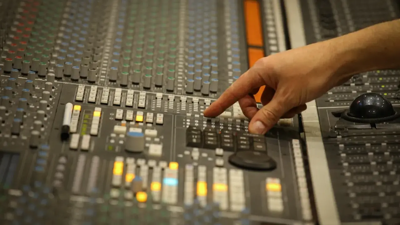 Main d'un ingénieur du son ajustant les faders d'une console de mixage, créant un son audio mono parfait.