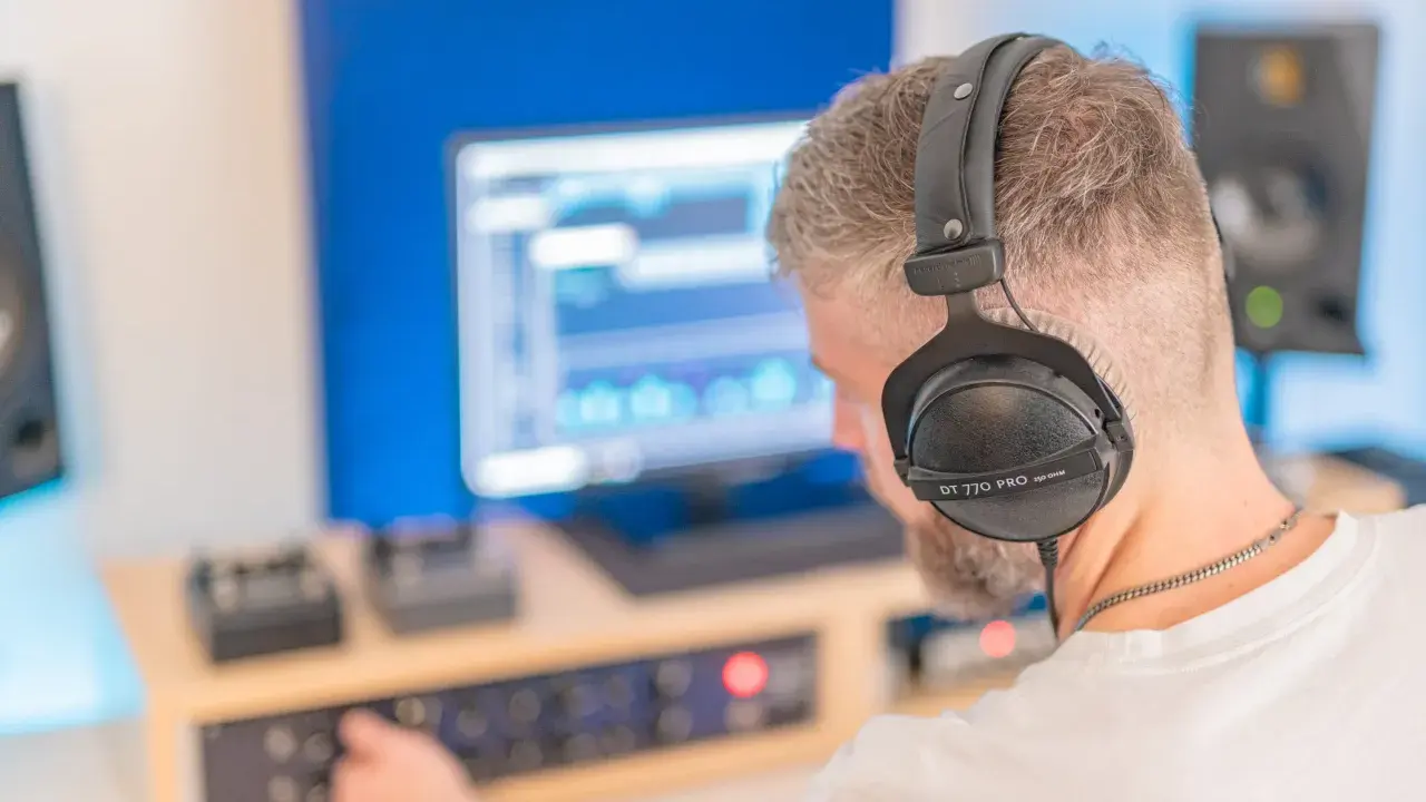 Un homme avec un casque sur les oreilles ajuste les réglages sur une console pour faire un EP dans son studio d'enregistrement.