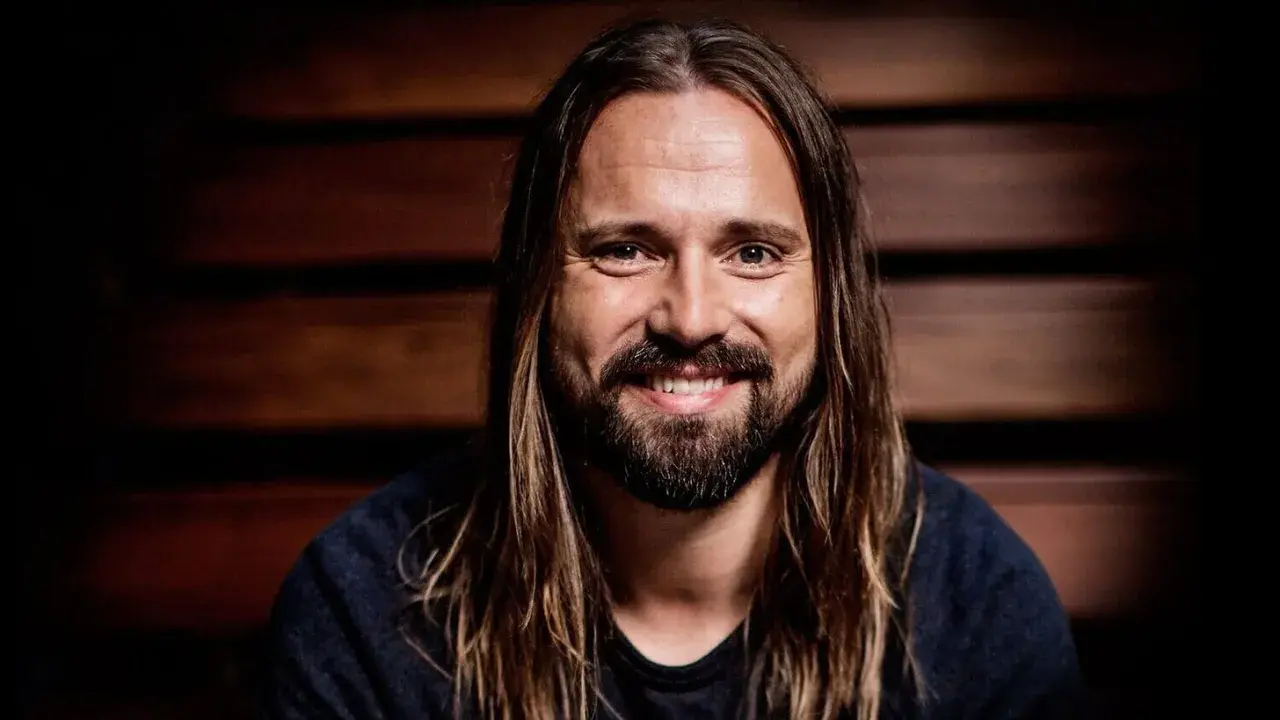 Un homme souriant aux longs cheveux bruns et à la barbe, peut-être un des compagnons d'écriture de Max Martin.