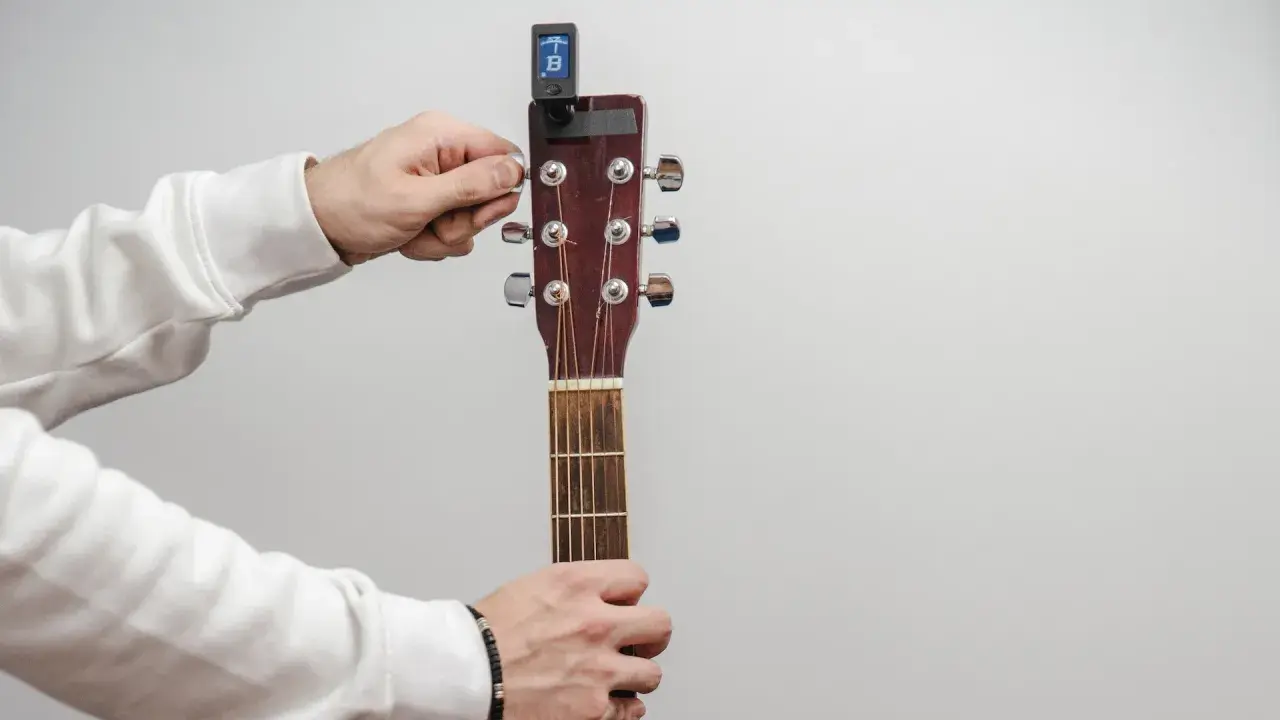 Main tenant de la guitare, il utilise un accordeur pour accorder l'instrument.