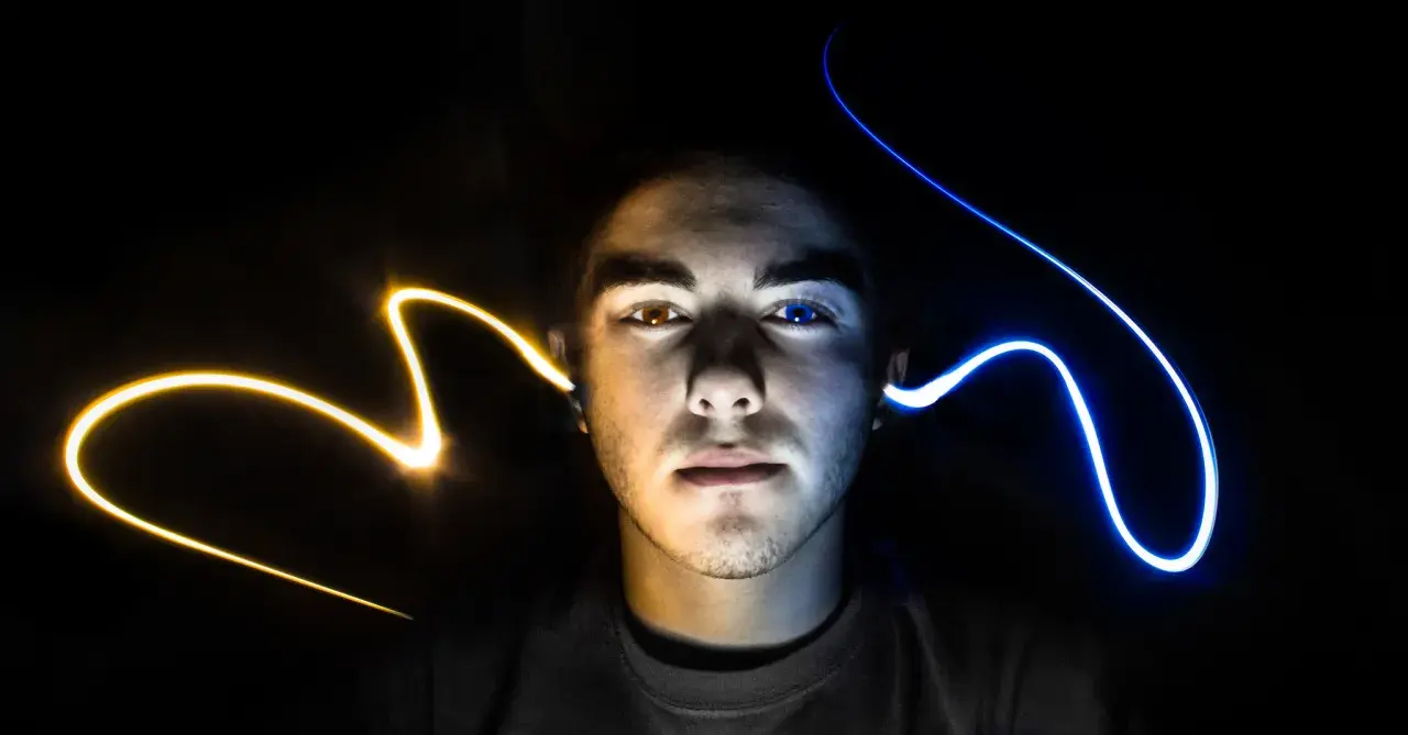 Visage d'un jeune homme éclairé par des traînées de lumière jaune et bleue, évoquant un ia mixage audio créatif.