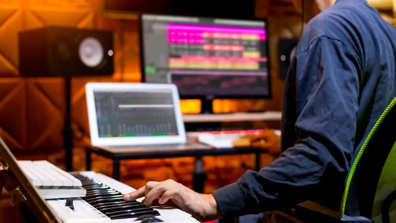 Un musicien compose avec un clavier et un ordinateur dans un studio d'enregistrement.