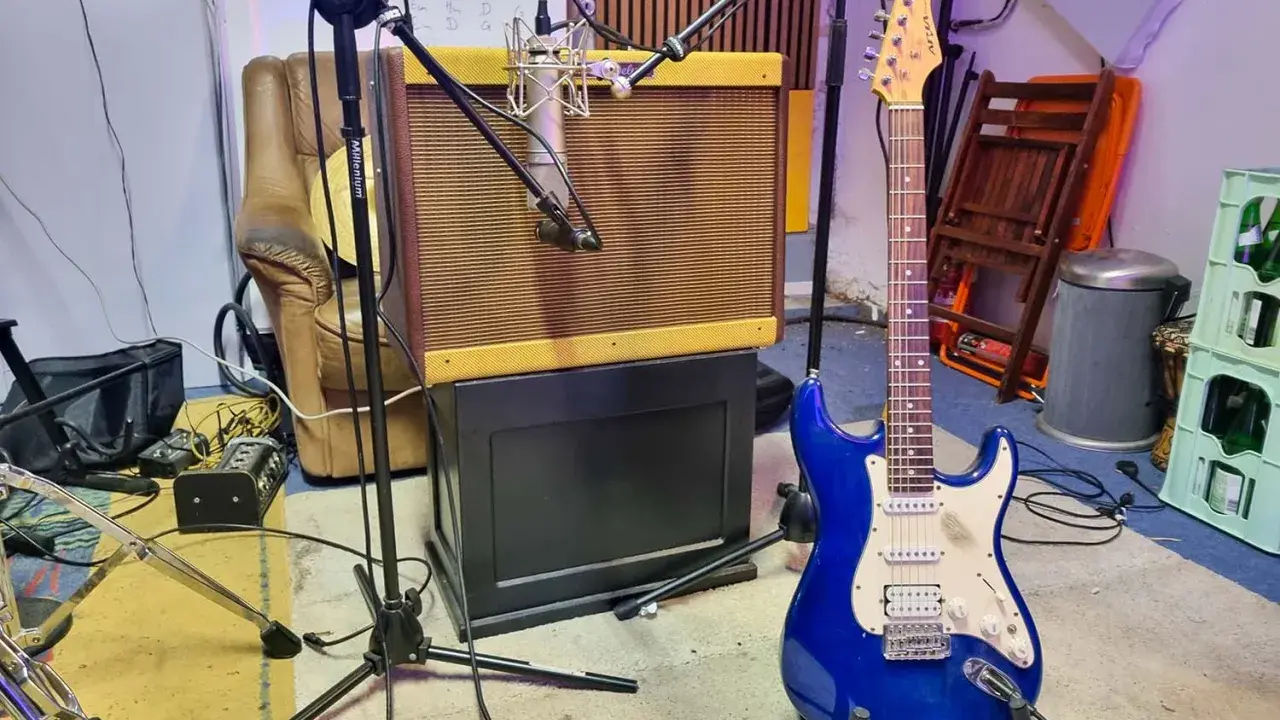 Une guitare électrique bleue étincelante est prête à jouer dans un studio d'enregistrement, à côté d'un ampli vintage et d'un fauteuil usé.