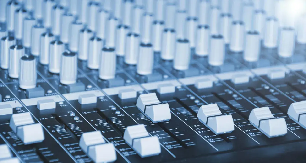 Vue rapprochée d'une console de mixage dans un studio de production musicale, avec ses potentiomètres et faders prêts à sculpter le son.