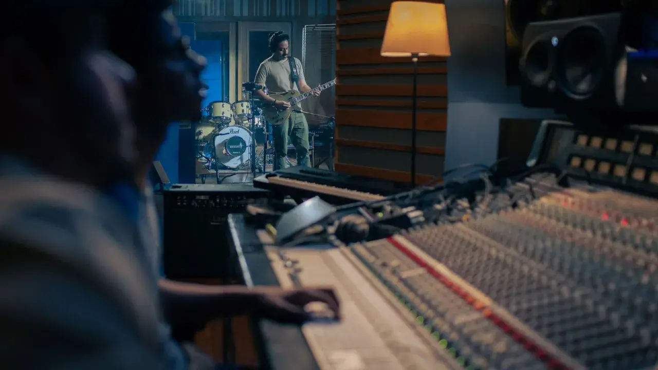 Un guitariste joue dans un studio d'enregistrement, tandis qu'un ingénieur du son est prêt à comment mixer la musique sur la console.
