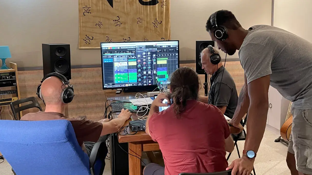 Trois hommes en formation mastering dans un studio d'enregistrement, concentrés sur un écran affichant une console de mixage numérique.