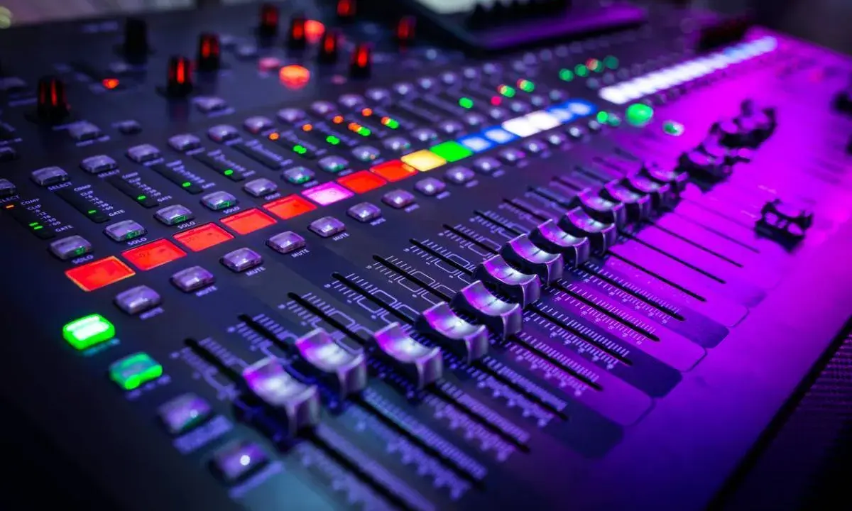 Gros plan sur un **mixer analogique** illuminé par des lumières violettes et rouges. Les faders et les boutons sont prêts pour une session d'enregistrement.