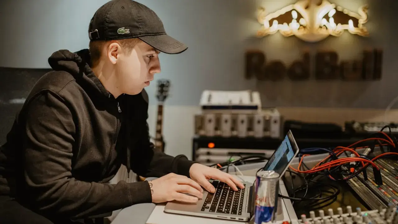 Un jeune homme travaille sur un ordinateur portable dans un studio d'enregistrement, avec le logo Red Bull en arrière-plan.