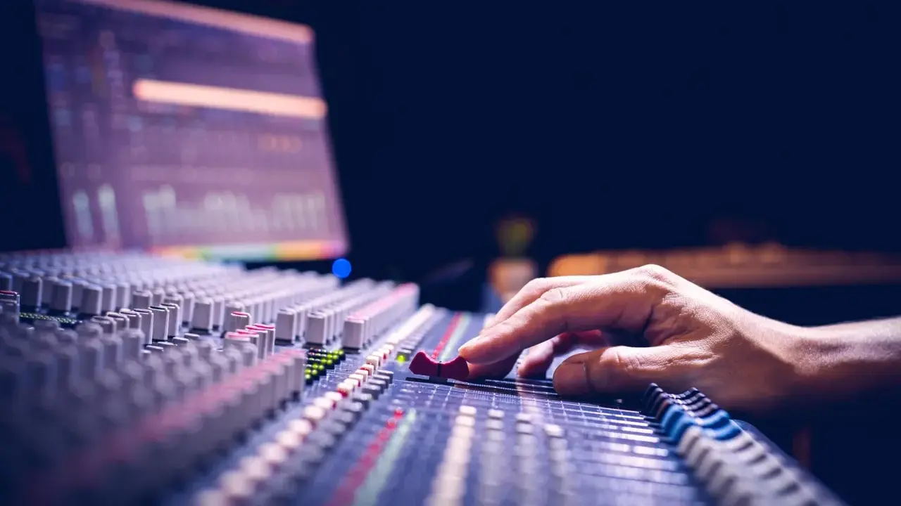 Main d'un ingénieur du son ajustant les curseurs d'une console de mixage pour optimiser la phase audio.