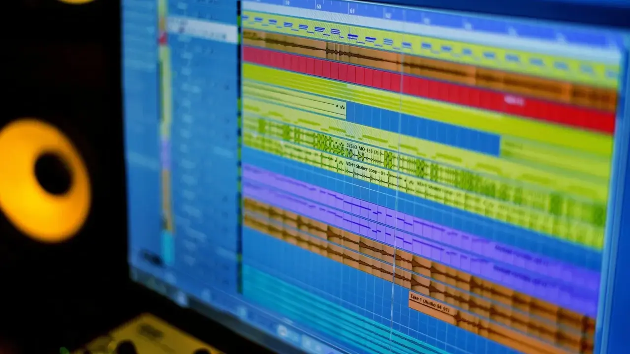 Écran d'ordinateur affichant une piste audio complexe, prêt pour le meilleur logiciel de mixage. Des moniteurs de studio sont visibles sur le côté.