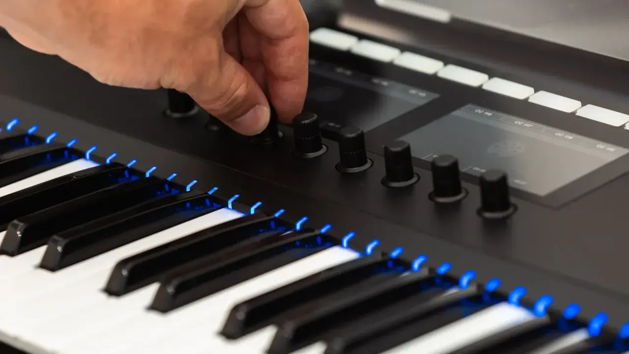 Main d'un musicien ajustant un bouton sur un clavier de musique numérique, avec des touches illuminées de bleu.