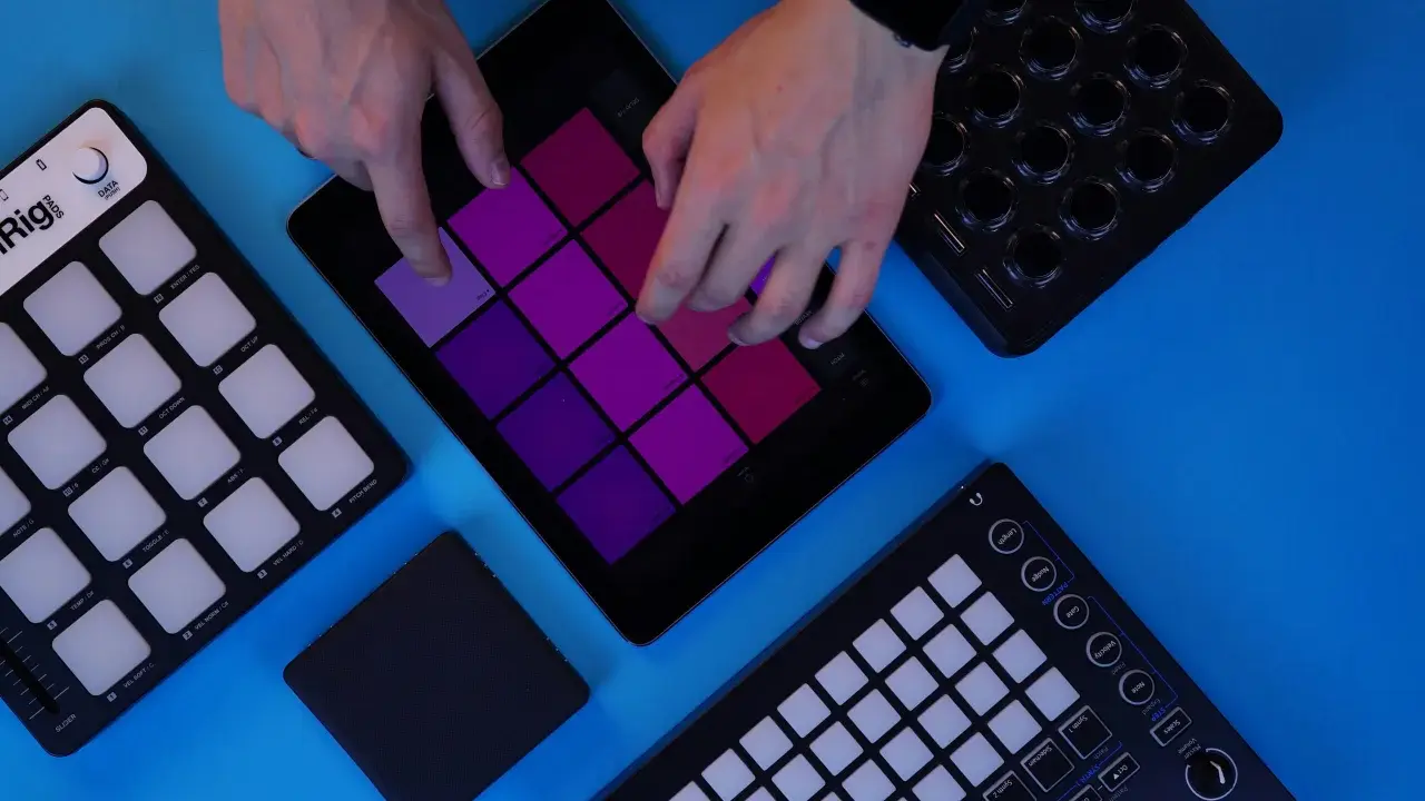 Des mains jouent sur une tablette avec des pads colorés, entourée de contrôleurs pour créer de la musique. Un sampler sans ordinateur en action.