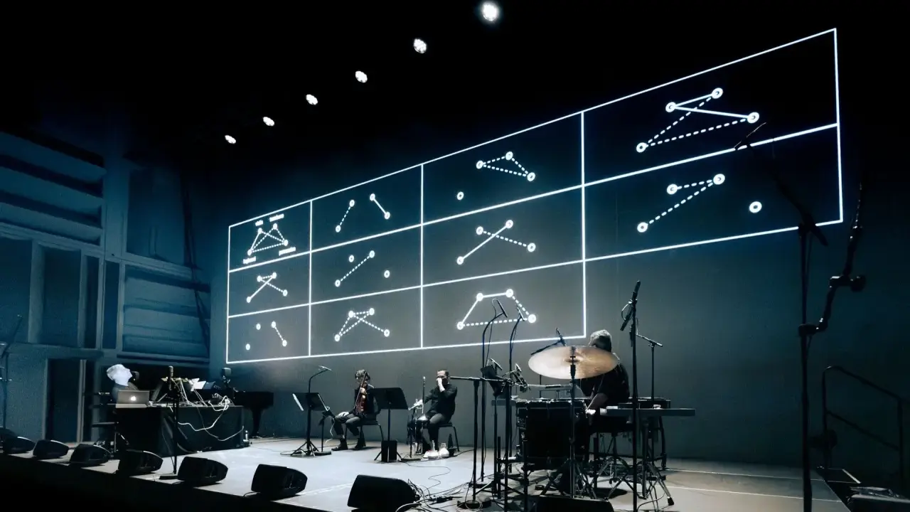 Sur scène, des musiciens jouent devant un écran projetant des schémas lumineux. Une performance pour comment se faire remarquer.