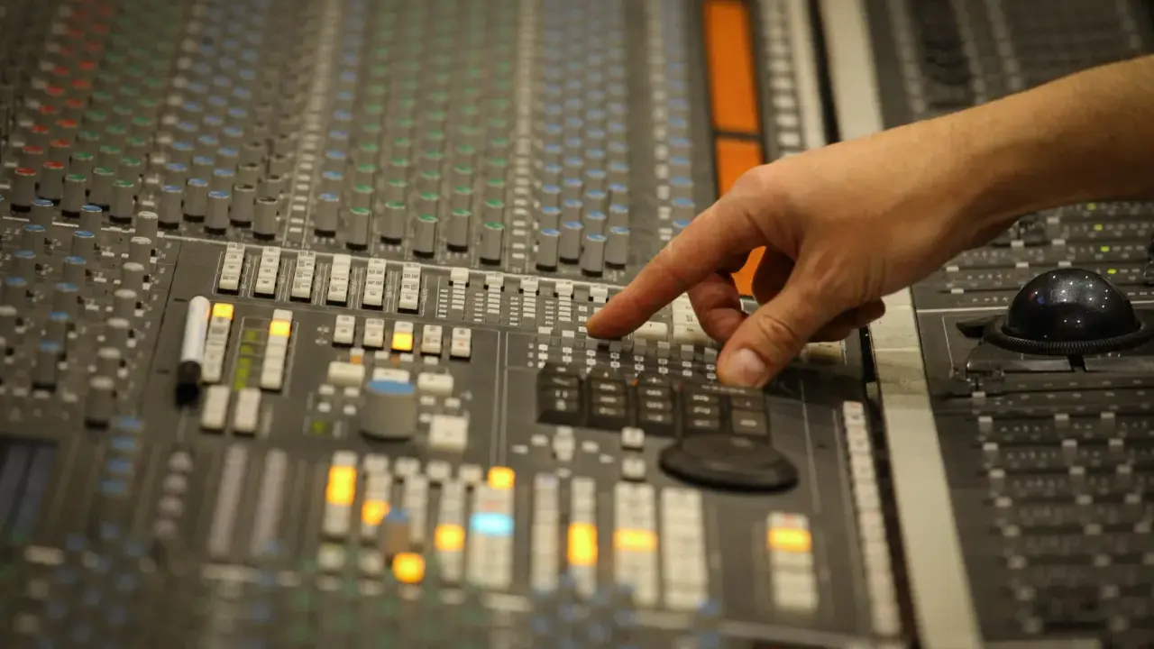 Main d'un ingénieur du son ajustant les faders d'une console de mixage pour un son stéréo parfait.
