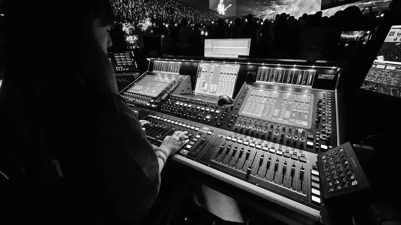 Une personne manipule une console de mixage dans un studio d'enregistrement, devant une foule lors d'un concert.