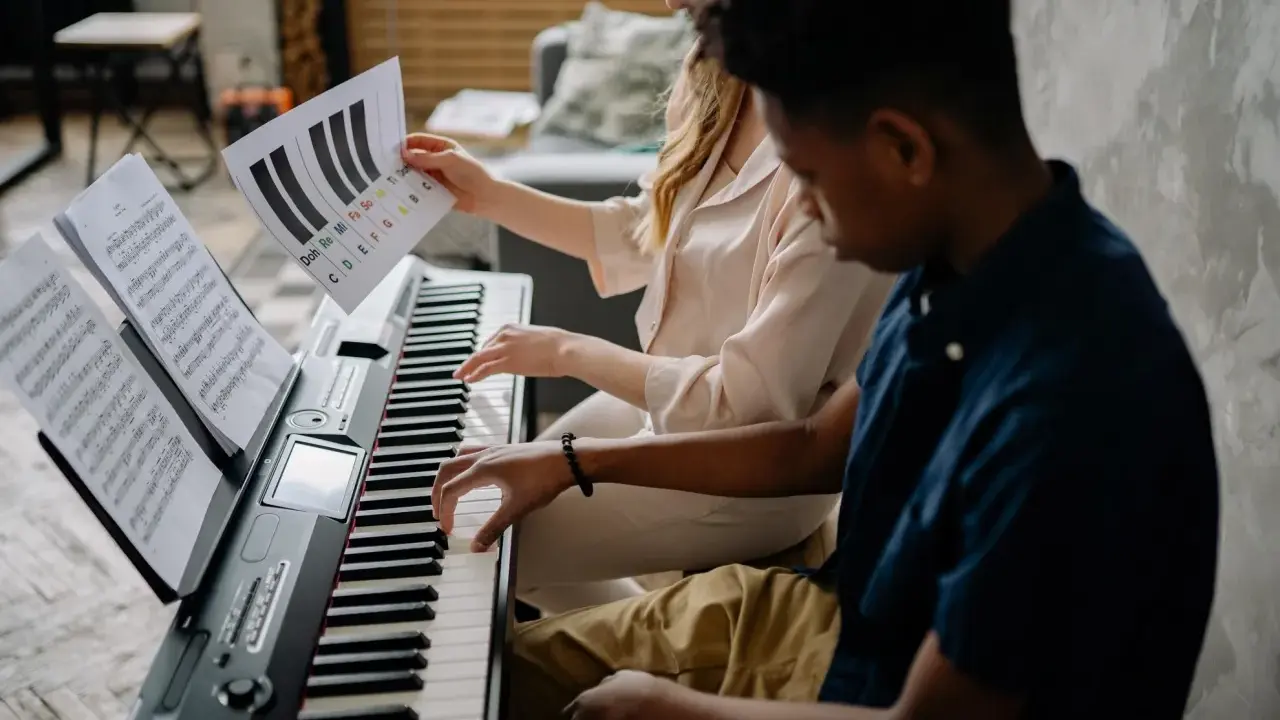 Deux jeunes jouent du piano, l'un tenant une partition montrant l'accord D7.