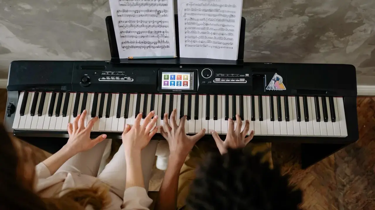 Deux mains jouent un accord c/b piano, des partitions sur le pupitre.