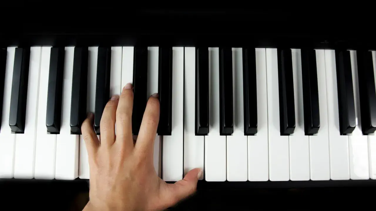 Main gauche jouant le sol 7 piano, doigts effleurant les touches noires et blanches.