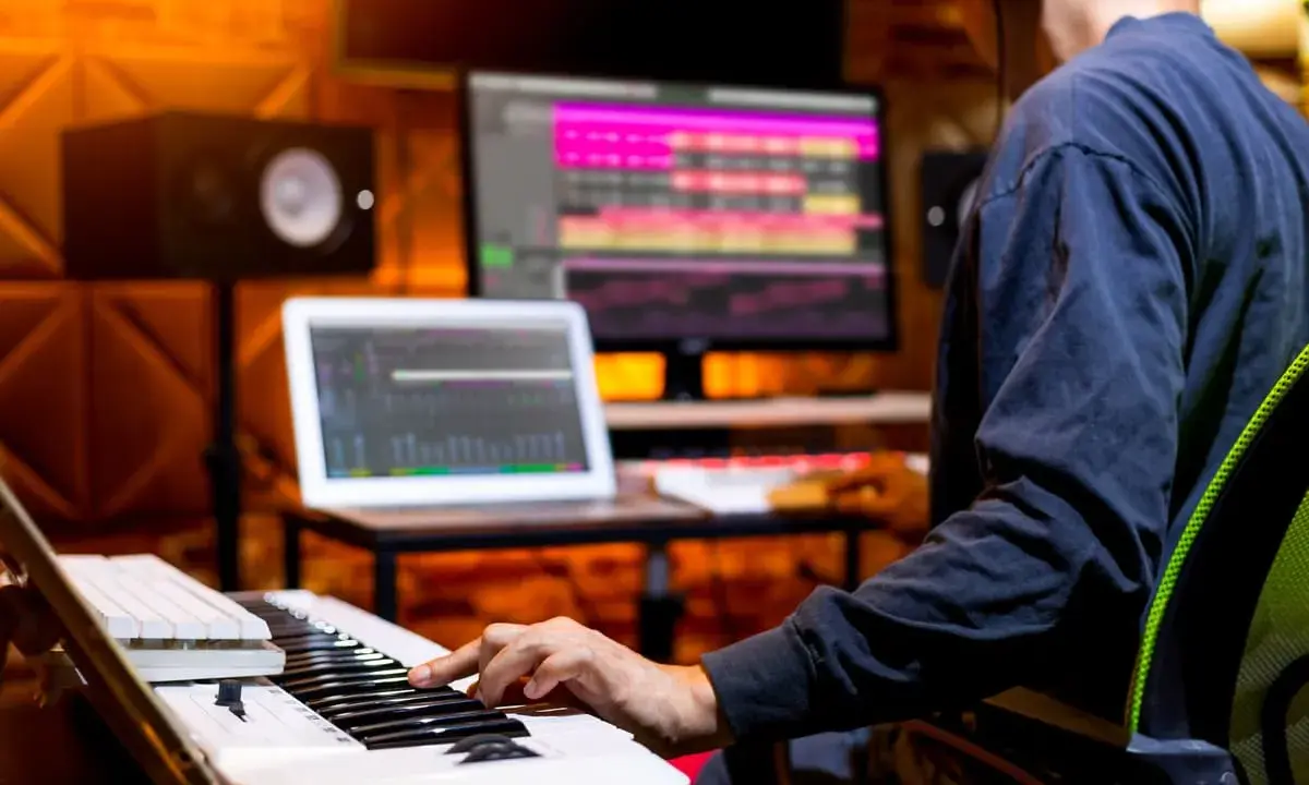Un musicien utilise un clavier et un ordinateur pour créer une composition musicale. L'application d'accompagnement musical est visible sur les écrans.