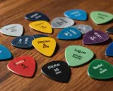 Un assortiment de médiators de guitare de différentes couleurs, chacun portant un nom ou un chiffre. Un médiator triangle jaune avec "Pecren & foop" est au centre.