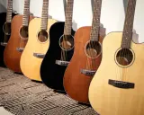 Une rangée de guitares acoustiques Cort, noires, marron et naturelles, posées sur un tapis rayé.