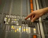 Main d'un ingénieur du son ajustant les faders d'une console de mixage, créant un son audio mono parfait.