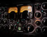 Gros plan sur un compresseur mastering avec deux VU-mètres lumineux et de nombreux boutons noirs.