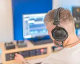 Un homme avec un casque sur les oreilles ajuste les réglages sur une console pour faire un EP dans son studio d'enregistrement.