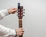 Main tenant de la guitare, il utilise un accordeur pour accorder l'instrument.