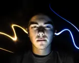 Visage d'un jeune homme éclairé par des traînées de lumière jaune et bleue, évoquant un ia mixage audio créatif.