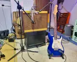 Une guitare électrique bleue étincelante est prête à jouer dans un studio d'enregistrement, à côté d'un ampli vintage et d'un fauteuil usé.
