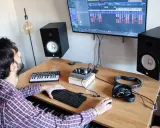 Un homme crée de la musique dans son studio. Il utilise un clavier, un ordinateur et des enceintes pour apprendre comment écrire un son.