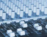 Vue rapprochée d'une console de mixage dans un studio de production musicale, avec ses potentiomètres et faders prêts à sculpter le son.