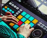 Mains d'un musicien jouant sur un instrument midi coloré, créant des rythmes avec les pads lumineux.
