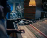 Un guitariste joue dans un studio d'enregistrement, tandis qu'un ingénieur du son est prêt à comment mixer la musique sur la console.