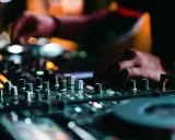 Mains d'un DJ en pleine action, manipulant les boutons pour apprendre à mixer. Lumières colorées et ambiance nocturne.