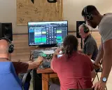 Trois hommes en formation mastering dans un studio d'enregistrement, concentrés sur un écran affichant une console de mixage numérique.