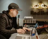 Un jeune homme travaille sur un ordinateur portable dans un studio d'enregistrement, avec le logo Red Bull en arrière-plan.