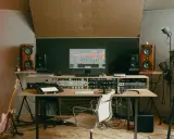 Un studio d'enregistrement avec des enceintes, un ordinateur affichant une station de travail audio numérique, des claviers, une guitare et divers équipements. C'est ici que le producteur de musique crée des sons.