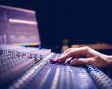 Main d'un ingénieur du son ajustant les curseurs d'une console de mixage pour optimiser la phase audio.