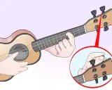 Main gauche sur le manche, main droite sur la tête pour accorder l'ukulele. Gros plan sur le réglage d'une corde.
