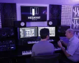 Deux hommes travaillent dans un studio d'enregistrement, le logo HEDAYAT MUSIC est visible sur un écran.