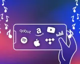 Une main tient un téléphone affichant les logos de diverses applications de musique : Qobuz, Amazon, YouTube, Spotify, Apple Music, Tidal. Des notes de musique flottent autour.