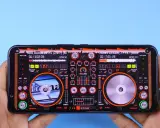 Mains DJ sur smartphone, avec une interface de mixage affichant deux platines et des contrôles. Un raccourci enregistrer est visible en haut à droite.