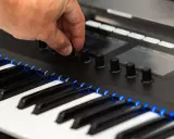 Main d'un musicien ajustant un bouton sur un clavier de musique numérique, avec des touches illuminées de bleu.