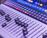 Console de mixage avec des curseurs et des boutons lumineux, prête pour une session d'enregistrement.