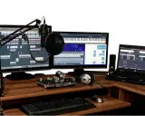 Postes de travail audio avec microphones, claviers, écrans affichant des logiciels de musique, et un ordinateur portable.